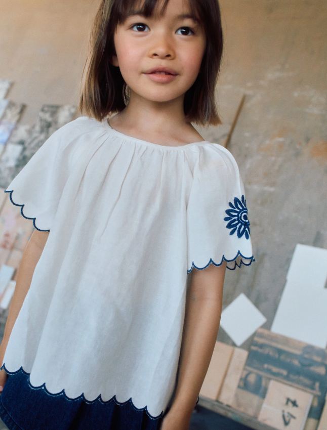 Blusa infantil con bordado y mangas onduladas.